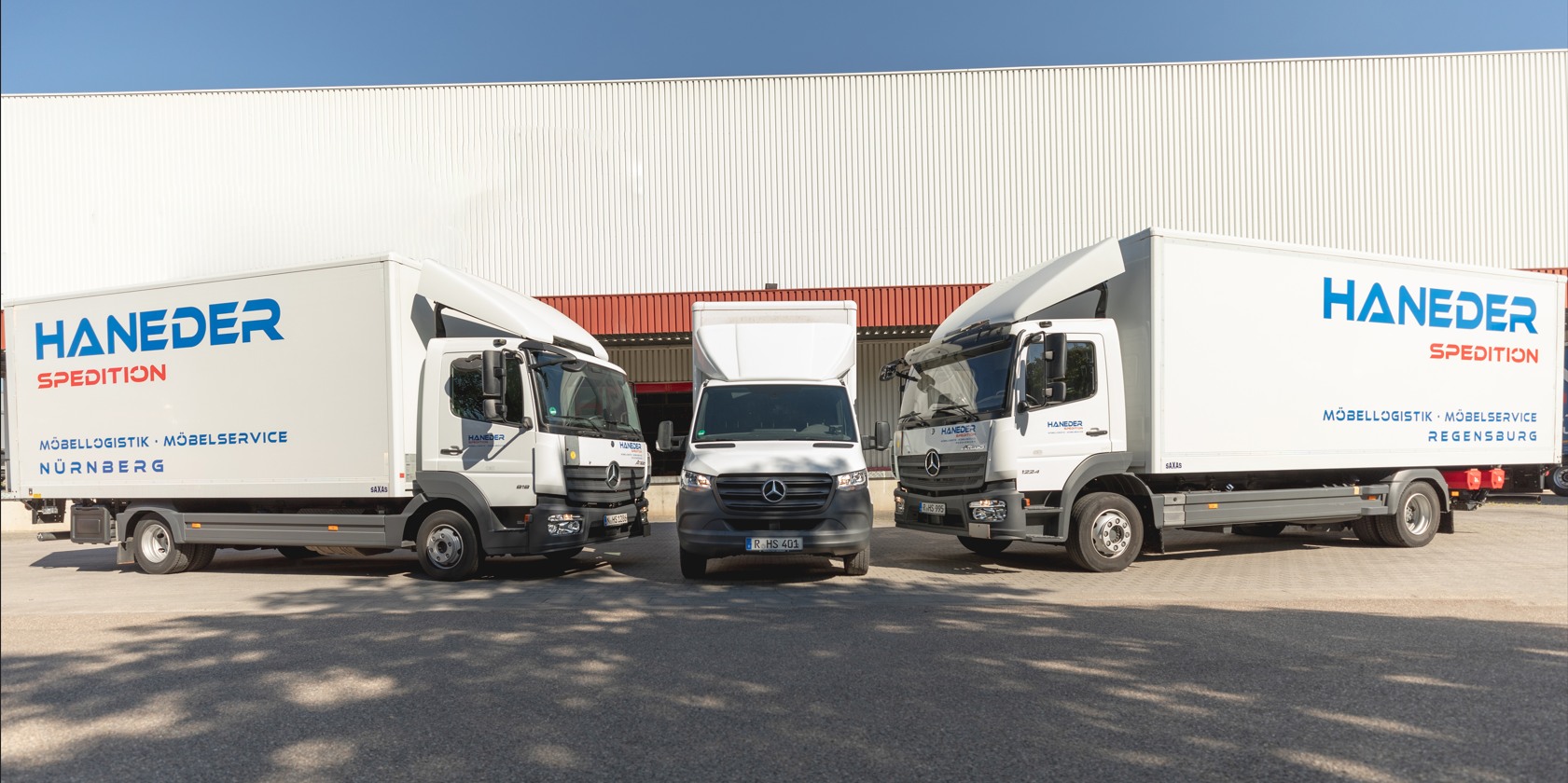 Zwei Atego und ein Sprinter der HANEDER Möbellogistik vor der Halle